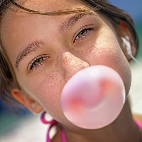 Close-up portrait of the teenager girl (age of 13) with freckles and iPod headphone makes bubble of chewing gum on the beach