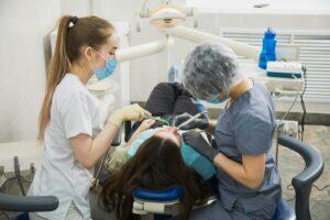 Female stomatologist curing dental cavity with assistant, patient on dentist chair.