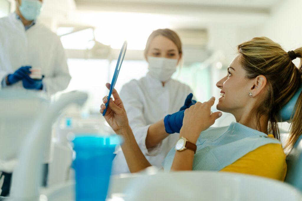 Dentist and patient in dentist office. Dentist holding prosthesis in background.