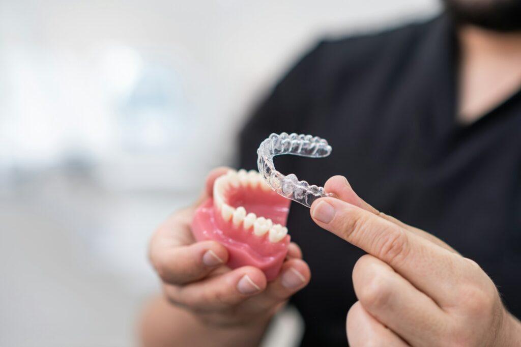 Doctor installing clear aligners on plastic lower human jaw to show simple and effective device