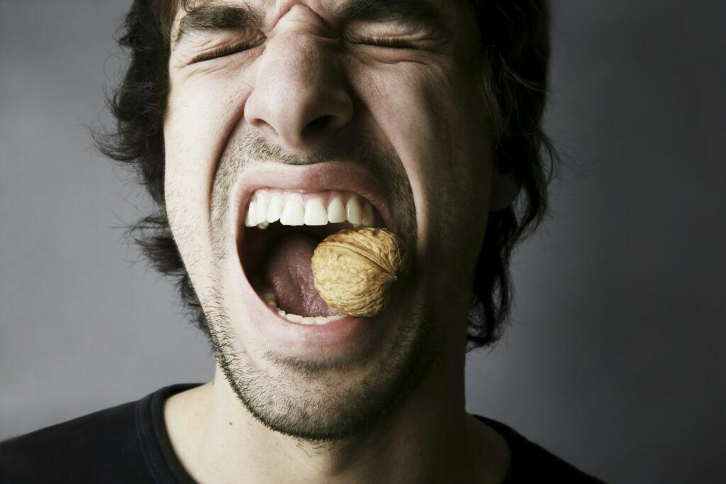 Portrait of young man trying to crack a walnut with his teeth, studio shot