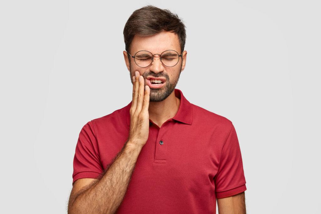 A man in a red polo shirt and glasses with a toothache