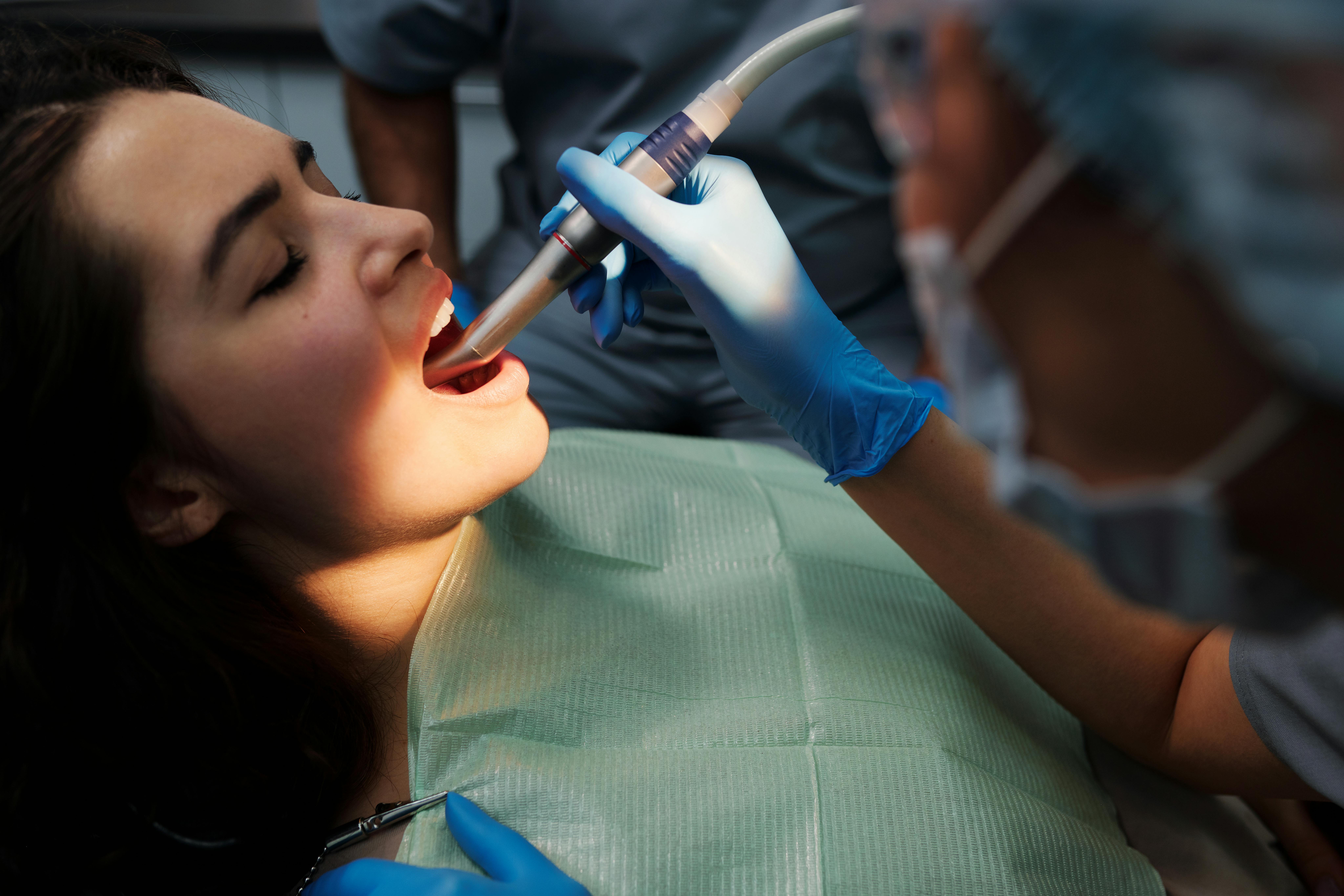 Dental hygienist using suction tool during a professional cleaning for a female patient in a dental chair, wearing a protective bib and gloves in a modern clinic setting.