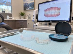 GET TO KNOW US 5 SureSmile aligners, aligner case, and retainer on a dental tray at an Orem, Utah dental office